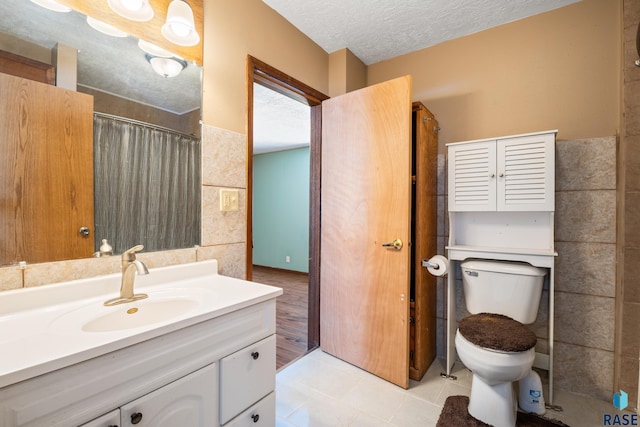 full bathroom with tile walls, toilet, a textured ceiling, vanity, and tile patterned floors