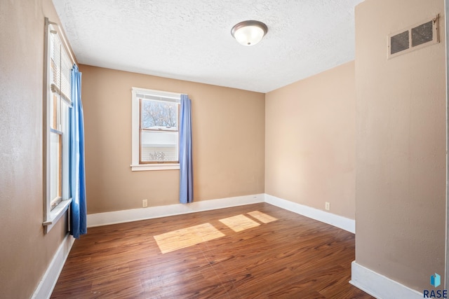 unfurnished room with wood finished floors, visible vents, and baseboards