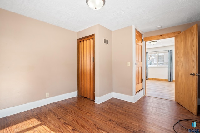 unfurnished bedroom with a textured ceiling, wood finished floors, visible vents, and baseboards