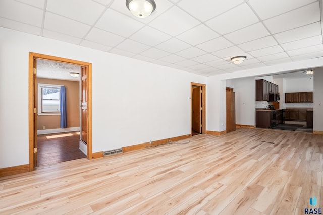 unfurnished living room featuring a paneled ceiling, light wood finished floors, baseboards, and visible vents