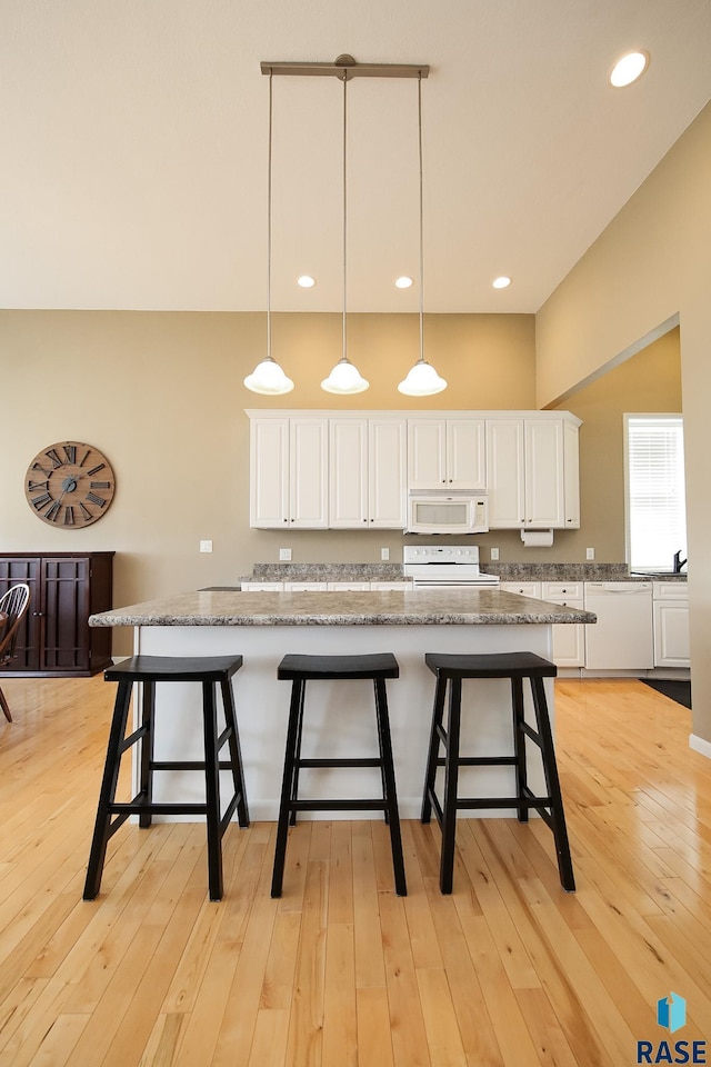 kitchen with white cabinets, white microwave, light wood-type flooring, a kitchen bar, and range with electric stovetop