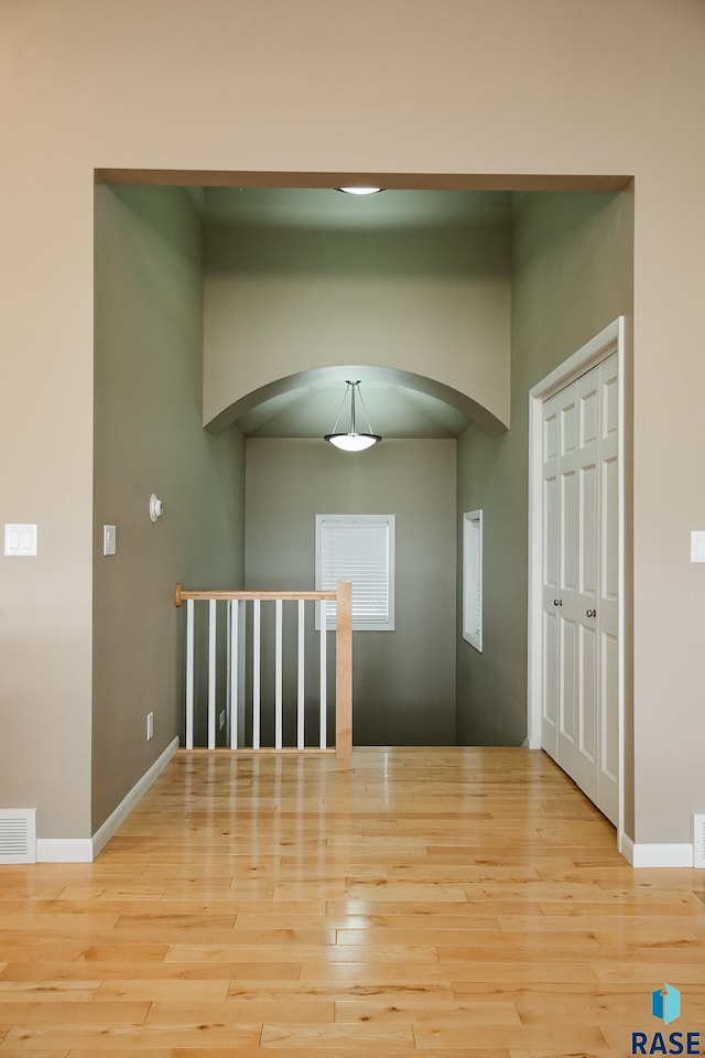 unfurnished room featuring baseboards, visible vents, arched walkways, and wood finished floors