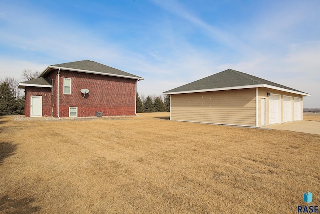 view of side of home featuring a detached garage, an outdoor structure, a lawn, and brick siding