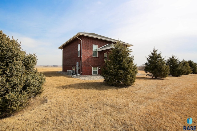 view of property exterior featuring brick siding, a lawn, and central AC