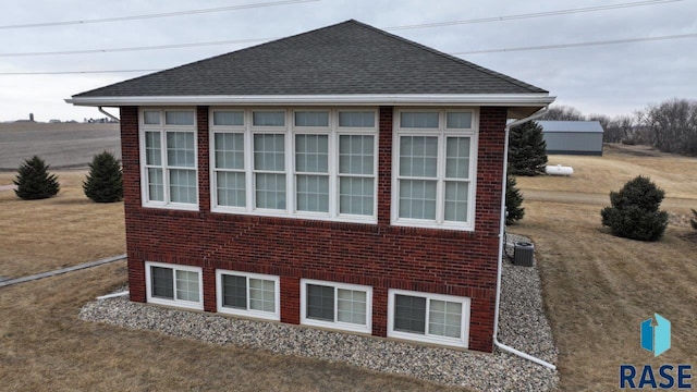 view of home's exterior with brick siding, roof with shingles, and cooling unit