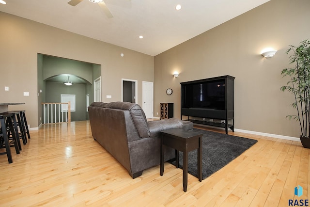 living room featuring arched walkways, ceiling fan, baseboards, and hardwood / wood-style flooring