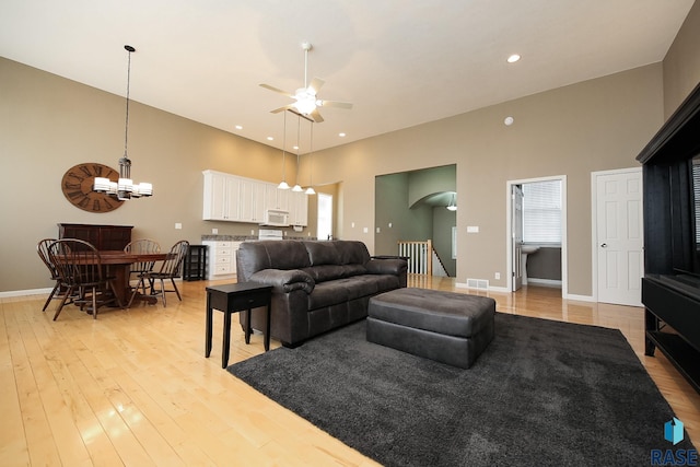 living room with light wood finished floors, baseboards, a towering ceiling, ceiling fan with notable chandelier, and recessed lighting