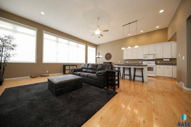 living area featuring recessed lighting, a towering ceiling, light wood-style flooring, ceiling fan, and baseboards