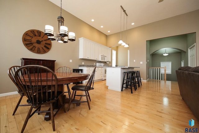 dining area with light wood-type flooring, baseboards, arched walkways, and a towering ceiling