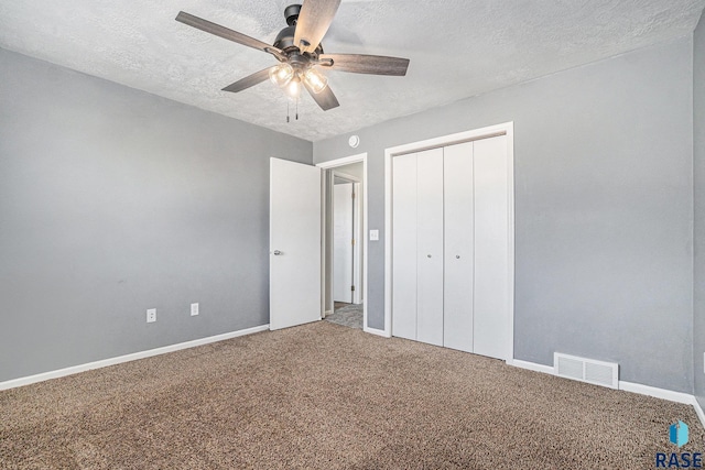 unfurnished bedroom with a textured ceiling, carpet floors, visible vents, baseboards, and a closet