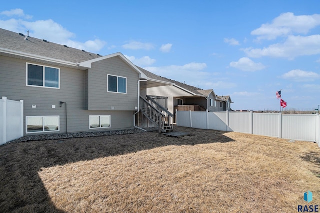 back of house with roof with shingles, a fenced backyard, a lawn, and stairs