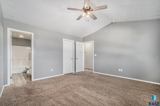 unfurnished bedroom featuring carpet flooring, vaulted ceiling, a textured ceiling, ensuite bath, and baseboards