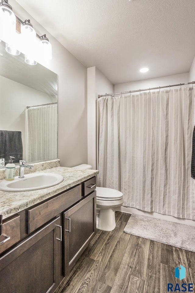 full bath with toilet, wood finished floors, curtained shower, a textured ceiling, and vanity