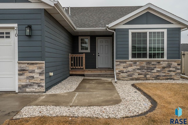 view of exterior entry featuring an attached garage, stone siding, and a shingled roof