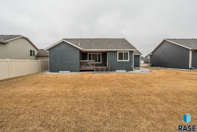 back of property featuring a shingled roof, a lawn, a wooden deck, and fence