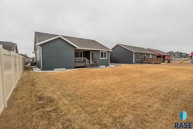 view of front of house with a shingled roof, a front yard, a wooden deck, and fence