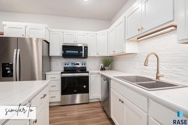 kitchen with stainless steel appliances, white cabinetry, a sink, and wood finished floors