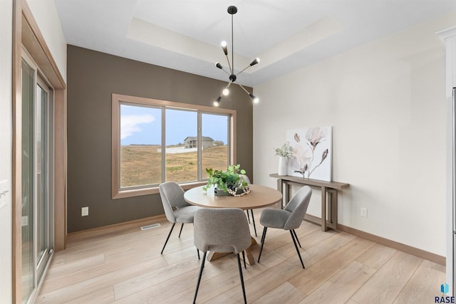 dining room with light wood-style flooring, a raised ceiling, visible vents, and baseboards