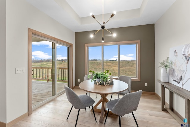 dining space featuring light wood-type flooring, an inviting chandelier, baseboards, and a tray ceiling