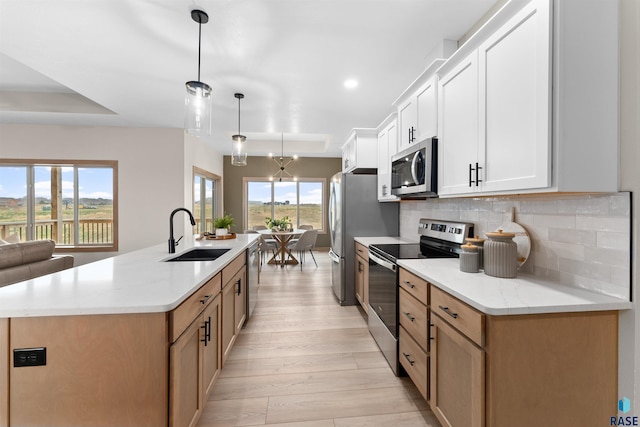 kitchen featuring a sink, appliances with stainless steel finishes, light wood-type flooring, tasteful backsplash, and a center island with sink