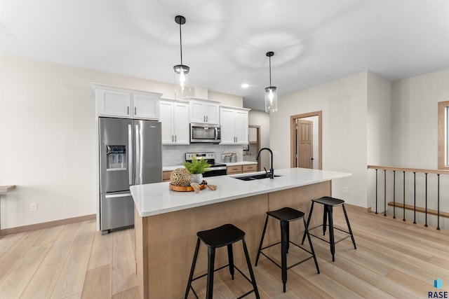 kitchen with light wood-style flooring, stainless steel appliances, a sink, a kitchen breakfast bar, and tasteful backsplash