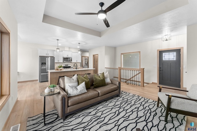 living room featuring a tray ceiling, light wood-style flooring, visible vents, and baseboards