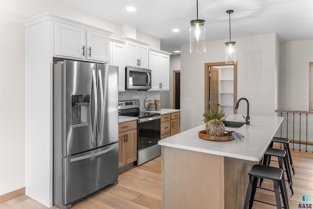 kitchen featuring a sink, a kitchen breakfast bar, light wood-style floors, appliances with stainless steel finishes, and an island with sink