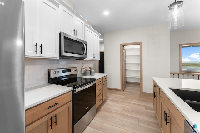 kitchen with pendant lighting, light wood-style flooring, backsplash, appliances with stainless steel finishes, and white cabinetry