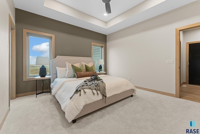 bedroom featuring light carpet, a raised ceiling, a ceiling fan, and baseboards