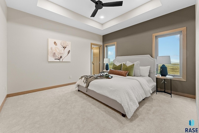 bedroom with light carpet, baseboards, and a raised ceiling