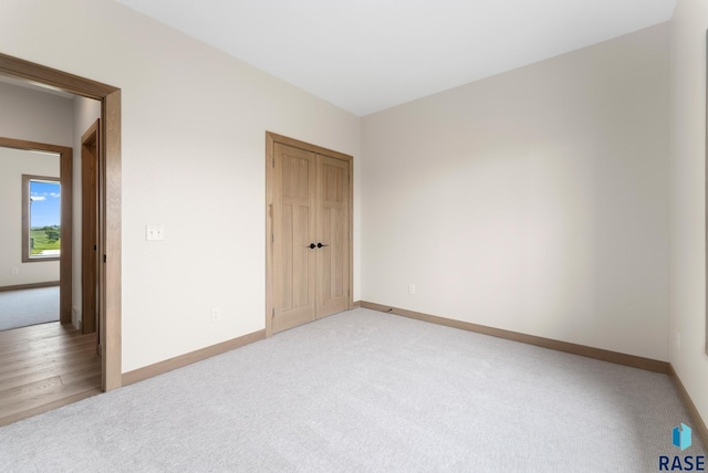 unfurnished bedroom featuring baseboards, a closet, and light colored carpet