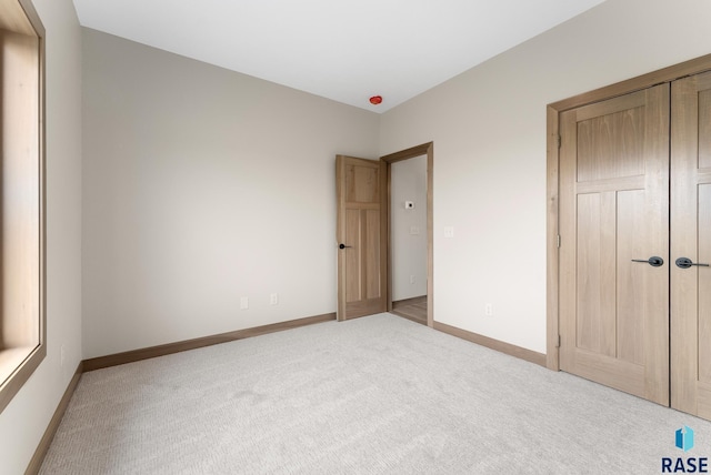 unfurnished bedroom featuring baseboards, a closet, and light colored carpet