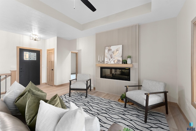 living room featuring baseboards, a tray ceiling, ceiling fan with notable chandelier, and light wood-style floors