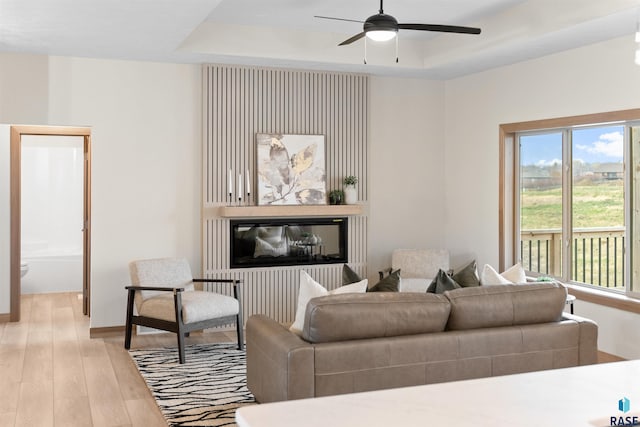 living area featuring a ceiling fan, a raised ceiling, baseboards, and wood finished floors