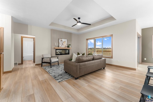 living area with light wood-style floors, baseboards, a tray ceiling, and a ceiling fan