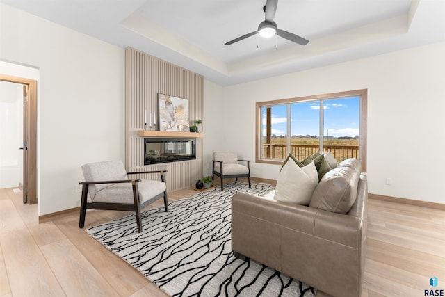 living area featuring light wood-style floors, baseboards, a tray ceiling, and a multi sided fireplace