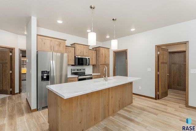 kitchen featuring light countertops, appliances with stainless steel finishes, light wood-style floors, a kitchen island with sink, and a sink