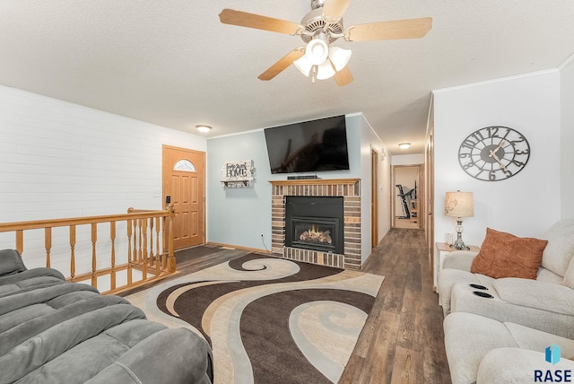 living area with ornamental molding, a ceiling fan, a brick fireplace, a textured ceiling, and wood finished floors