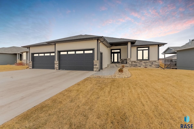 prairie-style house featuring a garage, stone siding, a yard, concrete driveway, and stucco siding