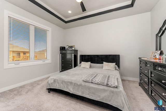 bedroom featuring baseboards, a raised ceiling, and light colored carpet