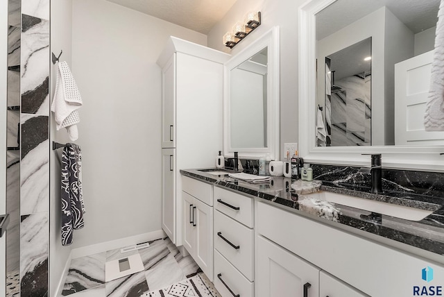 full bath featuring marble finish floor, a sink, baseboards, and double vanity