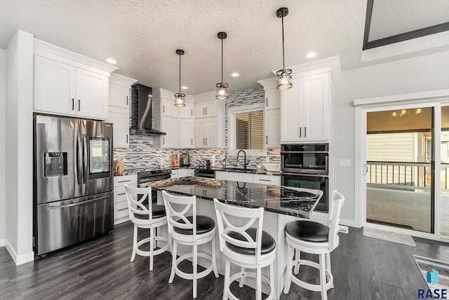 kitchen with stainless steel appliances, white cabinets, a sink, and wall chimney exhaust hood