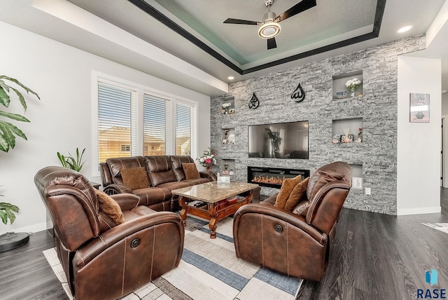 living area featuring a tray ceiling, a fireplace, baseboards, and wood finished floors