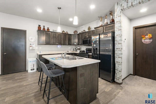 kitchen featuring a sink, dark brown cabinets, appliances with stainless steel finishes, light countertops, and a center island with sink