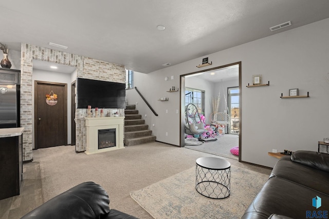 living room featuring baseboards, visible vents, a glass covered fireplace, stairs, and carpet flooring