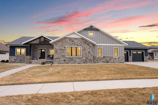 view of front of home featuring a yard, an attached garage, board and batten siding, stone siding, and driveway