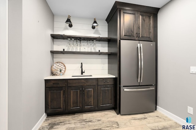 bar featuring baseboards, freestanding refrigerator, a sink, light wood-style floors, and indoor wet bar