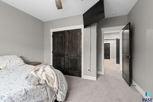 bedroom with a barn door, baseboards, a ceiling fan, light colored carpet, and a closet