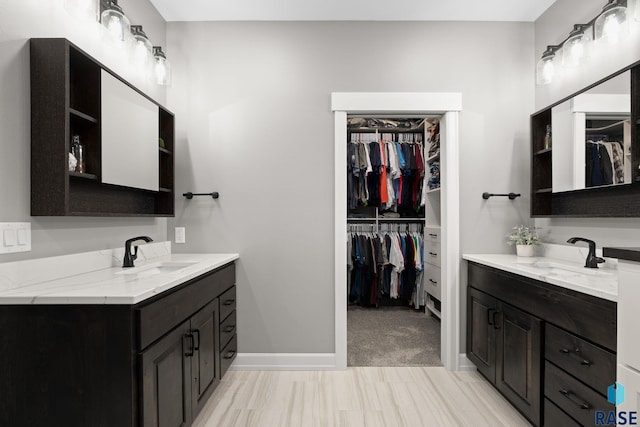 full bathroom with two vanities, a sink, a spacious closet, and baseboards