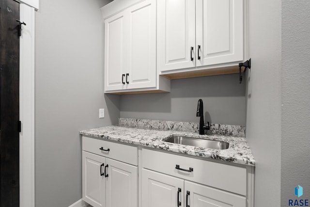 kitchen with light stone counters, white cabinets, and a sink